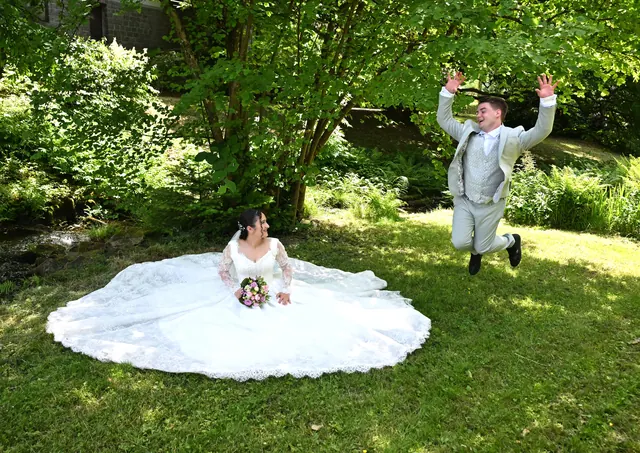 Bräutigam springt vor Freude hinter der Braut im ausgebreiteten Kleid