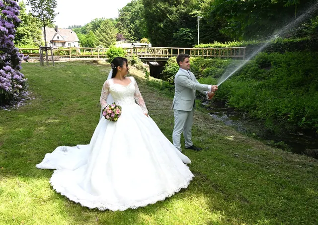 Bräutigam lässt den Sekt spritzen, Braut lacht im Park